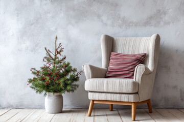 Obraz premium Interior setting features a plush upholstered armchair next to a small evergreen plant adorned with berries against a textured wall