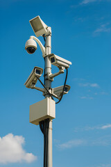 Multiple security cameras mounted on a pole against a bright blue sky.