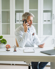 Doctor having phone call reading documents in clinic