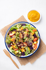 Healthy vegetable salad with lettuce, quinoa seed, azuki bean, corn, tomato, pumpkin and purple sweet potato in a bowl and pumpkin dressing on white background. Vegan and plant-based food