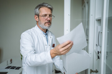 Fototapeta premium Mature male doctor organizing patient medical records in clinic