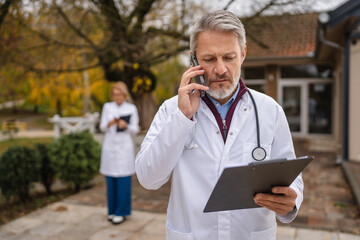 Senior doctor talking on phone while walking outdoors