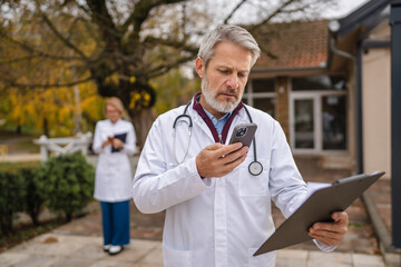 Doctor using smart phone outdoors checking medical records