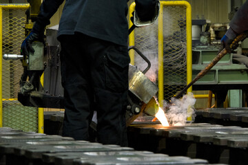 鋳物工場で鋳型に高温の融解鉄を注ぎ込む作業者
