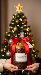 Hands holding panettone classico gift with red ribbon in front of christmas tree with lights