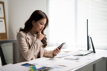 Asian businesswoman analyzing data using smartphone at office desk
