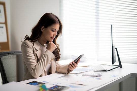 Asian businesswoman analyzing data using smartphone at office desk