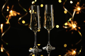 Happy New Year. Sparkling wine in flute glasses against sparklers and blurred lights on black background, bokeh effect