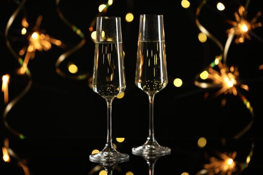 Happy New Year. Sparkling wine in flute glasses against sparklers and blurred lights on black background, bokeh effect
