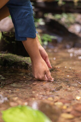 Close-up of a woman immersing her hands in a calm, shallow river. The image conveys serenity and connection with natural elements, emphasizing the refreshing sensation of water and the peaceful mood o