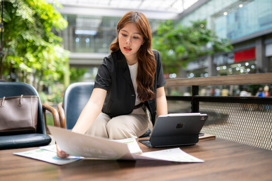 Asian businesswoman working outdoors checking business documents tablet - Powered by Adobe