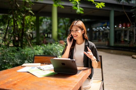 Asian businesswoman working remotely, talking on phone in cafe