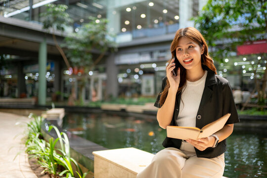 Asian businesswoman talking phone holding planner outdoor