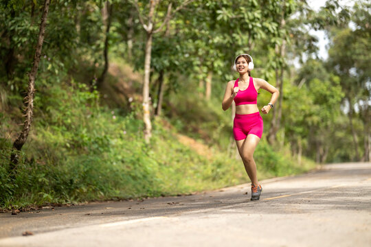 Asian woman running outdoors wearing headphones and smartwatch