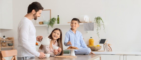 Happy father with his children pouring tea at table in kitchen