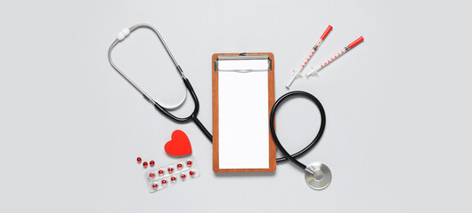 Blank clipboard with stethoscope, pills and syringes on grey background. World Health Day
