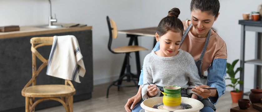 Little girl with her mother painting ceramic pot at home - Powered by Adobe