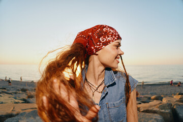 lifestyle woman with long red hair in modern boho-western denim street style smiling by the beach at sunset with warm film color tones and relaxed mood