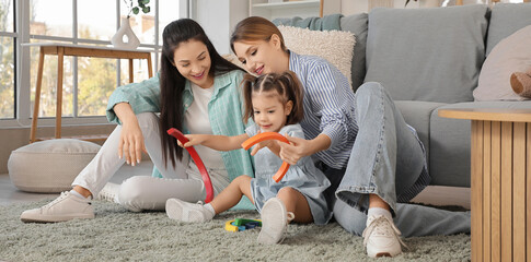 Young lesbian couple playing with their little daughter at home