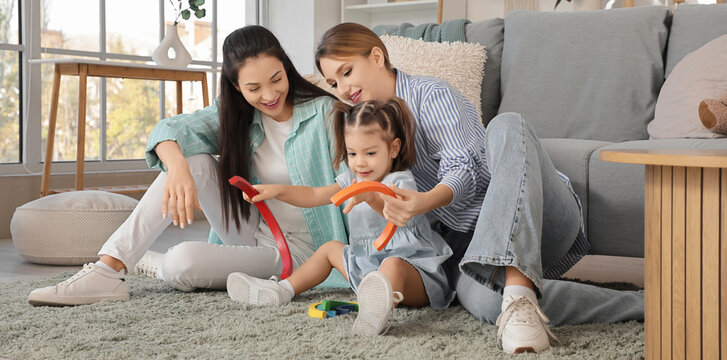 Young lesbian couple playing with their little daughter at home - Powered by Adobe