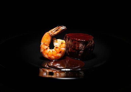 Gourmet grilled tiger prawn and beef steak with rich sauce on a reflective black surface