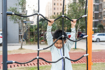 A young boy is actively climbing on a rope net in an outdoor park, engaging in physical play.