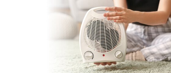 Woman with electric fan heater sitting on carpet at home, closeup