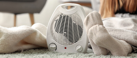 Electric fan heater and woman in warm socks at home, closeup