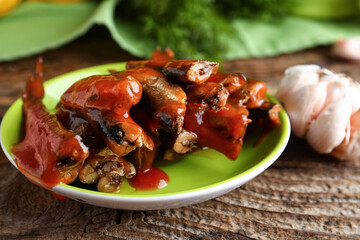 Plate with canned fish in tomato sauce and garlic on wooden table