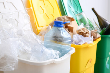 Trash bins with recycling symbol and different garbage near white wall