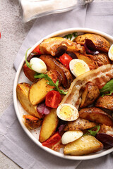 Plate of tasty potato salad with eggs, tomatoes and bacon on light background, top view