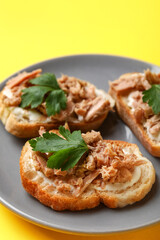 Plate with tasty tuna bruschettas on yellow background