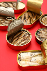 Opened tin cans with different fish on red background