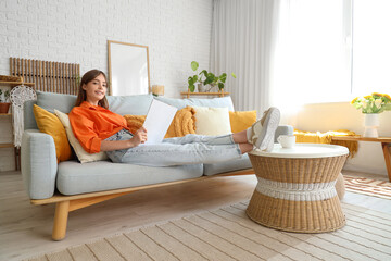 Pretty young woman reading magazine while relaxing on sofa
