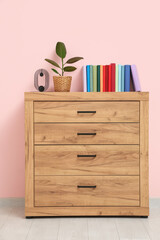 Wooden chest of drawers with books  and houseplant near pink wall