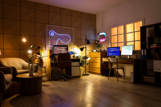 Interior of programmer's office with desks and glowing lamps at night - Powered by Adobe