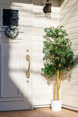 白い板張りの壁の家の玄関の扉と植木