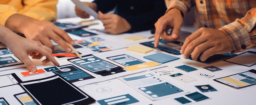 A diverse group of individuals engages in a creative design session, focused on developing user interface mockups and prototypes on a stylish table in a bright office space. SACTR - Powered by Adobe