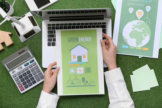Woman with papers, laptop, calculator and wind turbine on grass. Green Energy concept