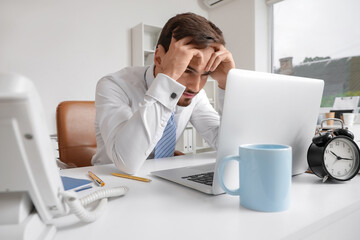 Stressed businessman working with laptop at table in office