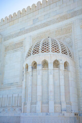 A detailed architectural photograph showcasing the intricate marble lattice dome and ornate Arabic calligraphy on the exterior wall of the Sultan Qaboos Grand Mosque in Muscat, Oman
