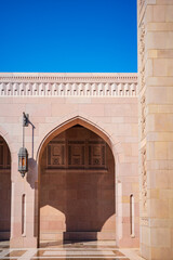 A minimal and elegant architectural photograph showcasing the arched sandstone corridor of the Sultan Qaboos Grand Mosque in Muscat, Oman. The image highlights traditional Islamic design elements