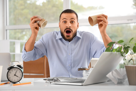 Stressed businessman with empty cups at table in office - Powered by Adobe