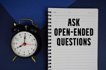 Ask Open-Ended Questions text written on notepad with alarm clock on blue background
