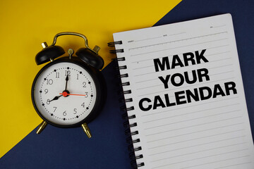 Mark Your Calendar text written on notepad with alarm clock on blue background