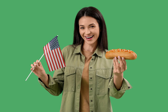 Young happy woman with tasty hot dog and flag of USA on green background