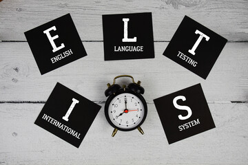 Obraz premium IELTS International English Language Testing System with alarm clock on wooden background