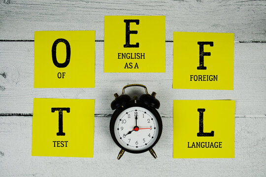 TOEFL Test of English as a Foreign Language with alarm clock on wooden background