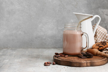 Mason jar of sweet chocolate milk and cocoa beans on grey background