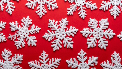 A close-up, top-down view of densely packed, overlapping white snowflake ornaments of various sizes, completely covering a red background. Creates a rich holiday texture or festive wallpaper.
